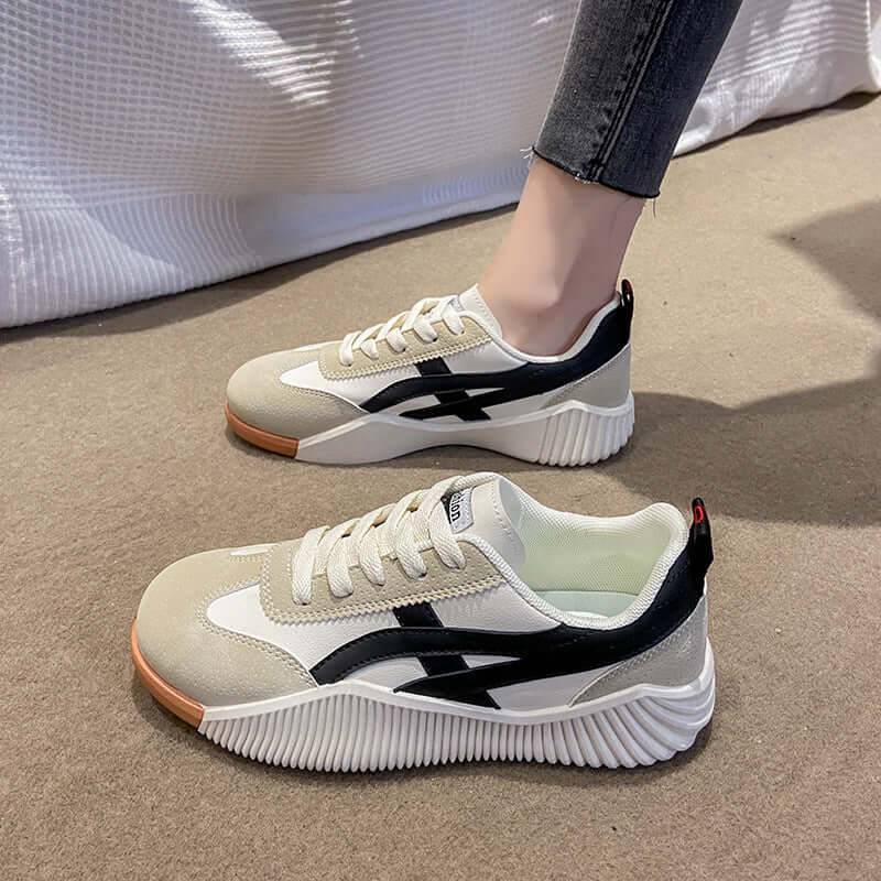 Women's feet wearing off-white and black chunky platform sneakers, showing the low-top profile, gum-tone outsole and lace-up closure from a front-side angle