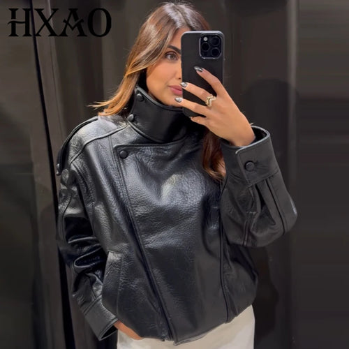Model taking a mirror selfie wearing an oversized black moto jacket with a high stand collar and snap-button closure