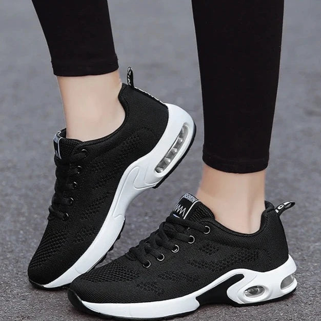 Black lace-up women's sneakers with white chunky midsole and air cushion windows, worn with black leggings, side view