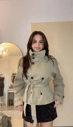 Front-facing view of women's short double-breasted trench jacket with self-tie belt and stand collar, styled with a patterned mini skirt