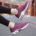 Purple women's lace-up sneakers with white midsole and air cushion sole windows, raised leg view on a street background
