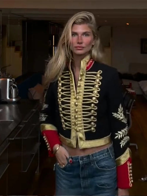 Model wearing a black cropped hussar jacket with gold passementerie front and red contrast cuffs, styled with jeans