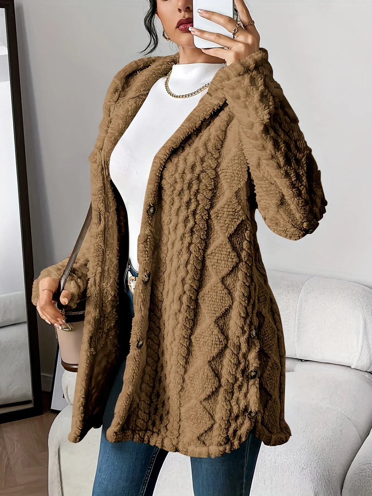 Mirror selfie view of a woman wearing an oversized hooded cardigan in camel brown with a raised diamond-texture surface, paired with a white turtleneck and jeans